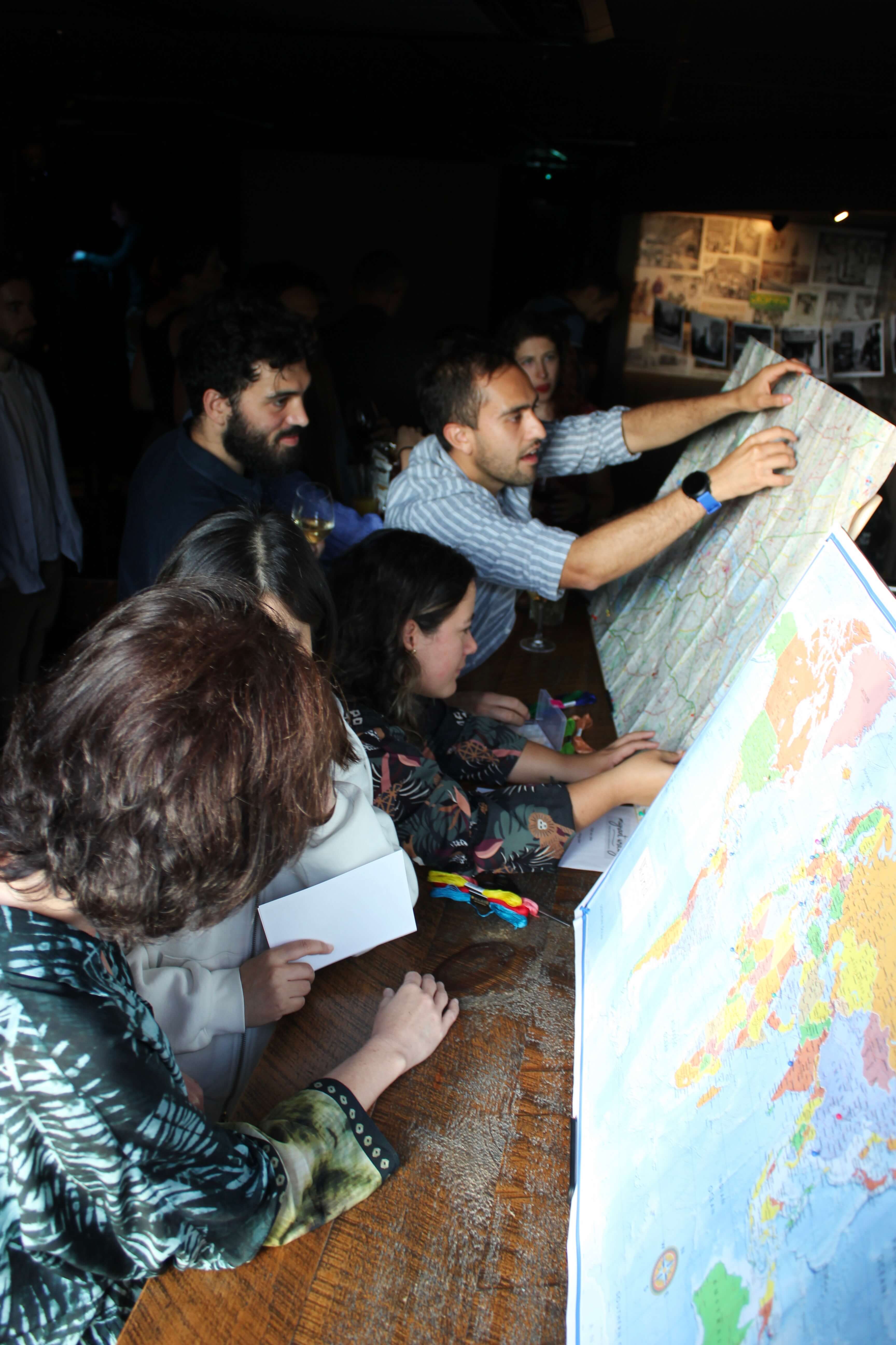 People talking and pinning locations on a map of London and a map of the world.